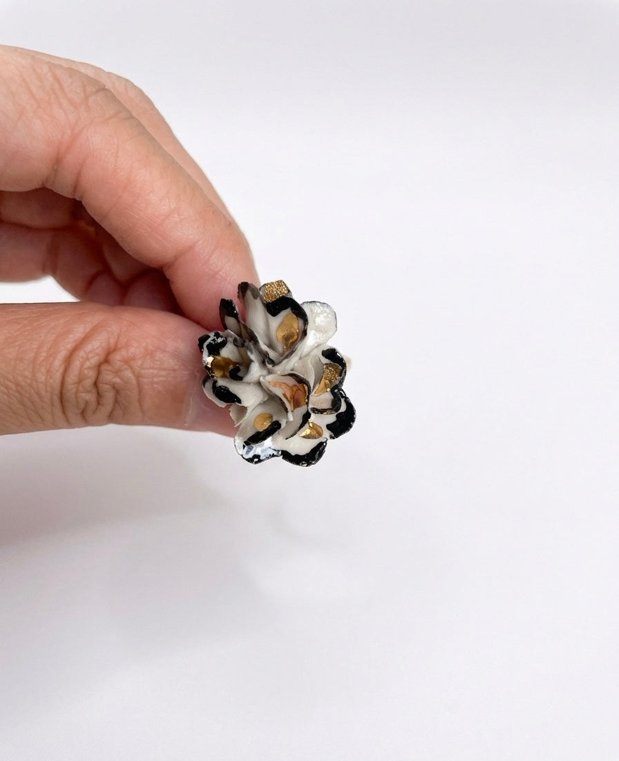 A hand holding a small black, white, and gold patterned ceramic flower