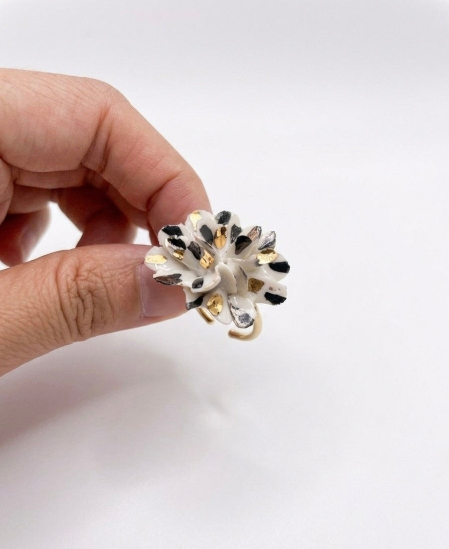 Hand holding a white ceramic flower ring with black and gold speckles