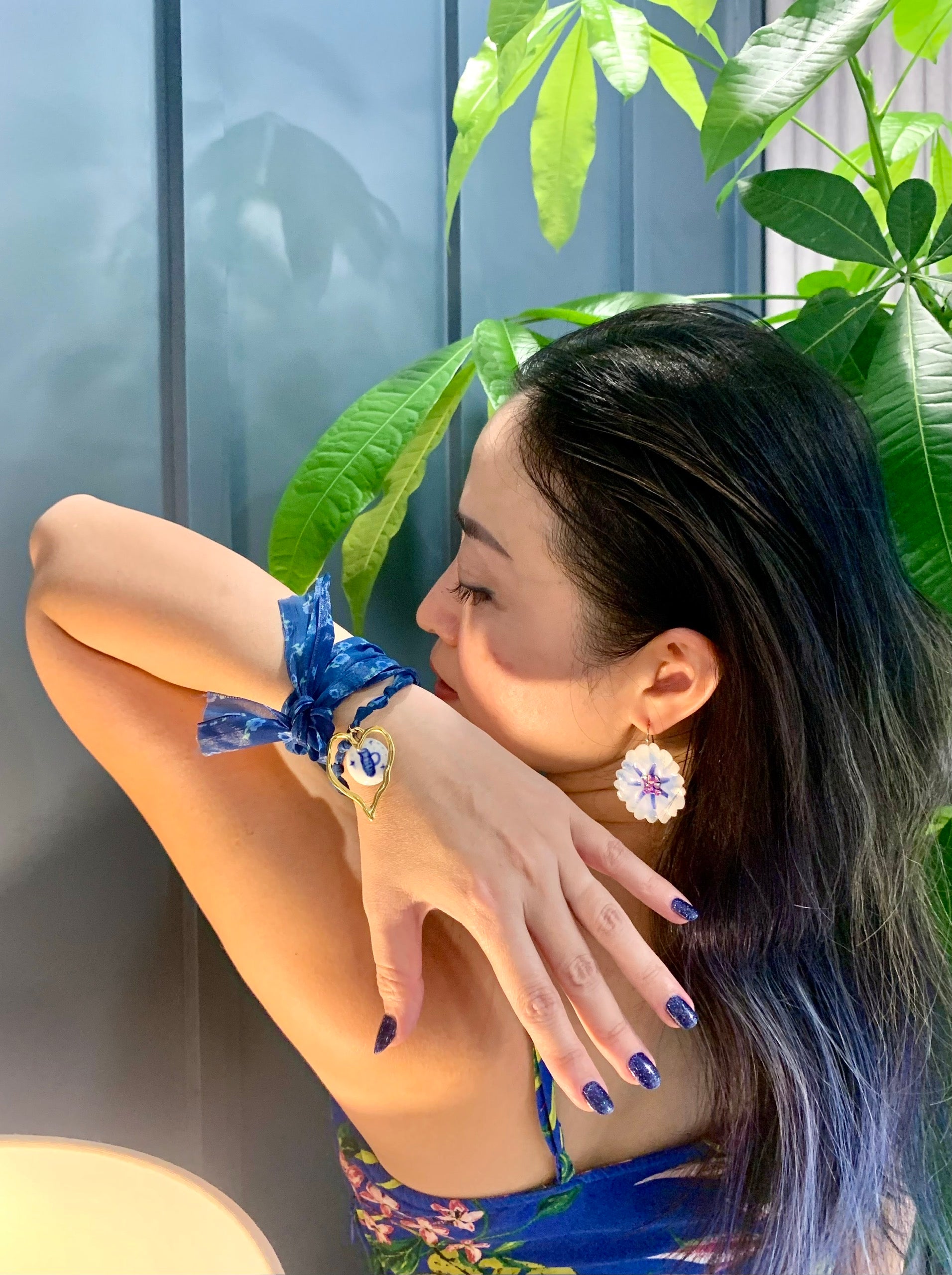 Người phụ nữ đeo hoa tai bông hoa trắng và vòng tay vải xanh gắn charm trái tim vàng