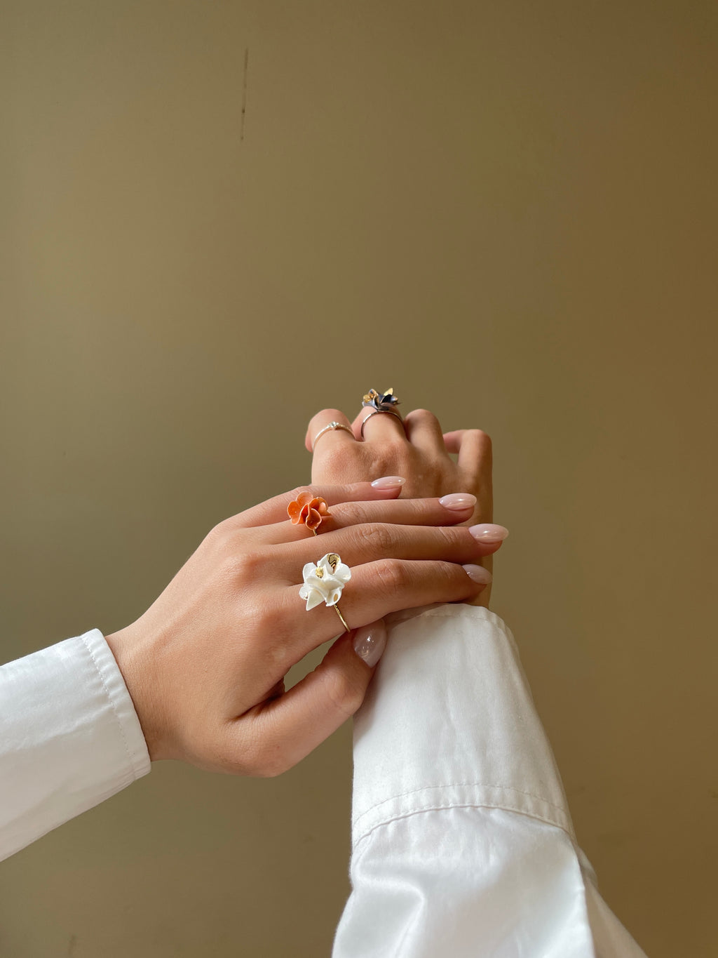 Hai bàn tay đeo nhẫn hoa trắng và cam nổi bật trên nền trung tính, phong cách nhẹ nhàng nữ tính
