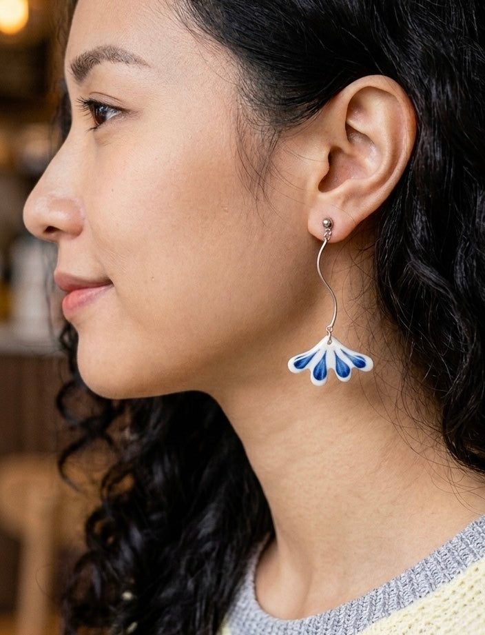Profile view of a woman wearing a silver earring with a blue and white petal shaped pendant
