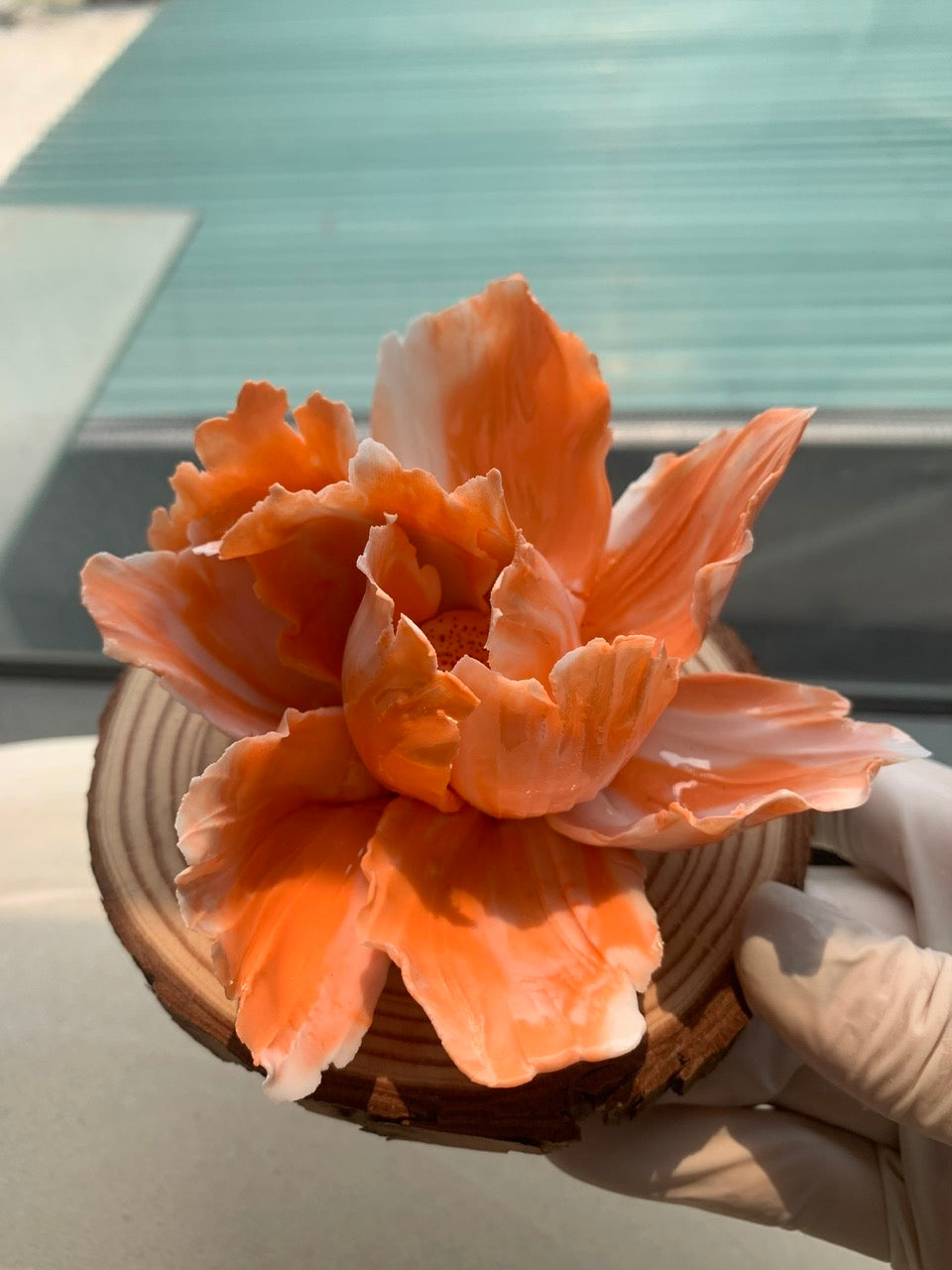 Handmade peach colored flower sculpture with white edges on a wooden disc