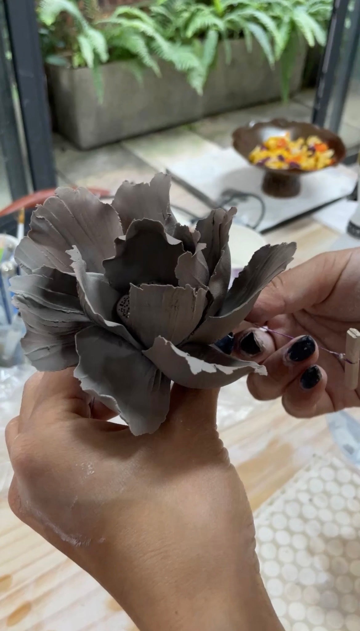 Hands holding a large, detailed grey clay flower sculpture